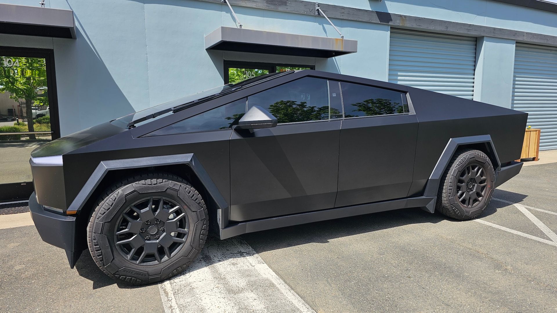 A black tesla cybertruck is parked in a parking lot in front of a building.