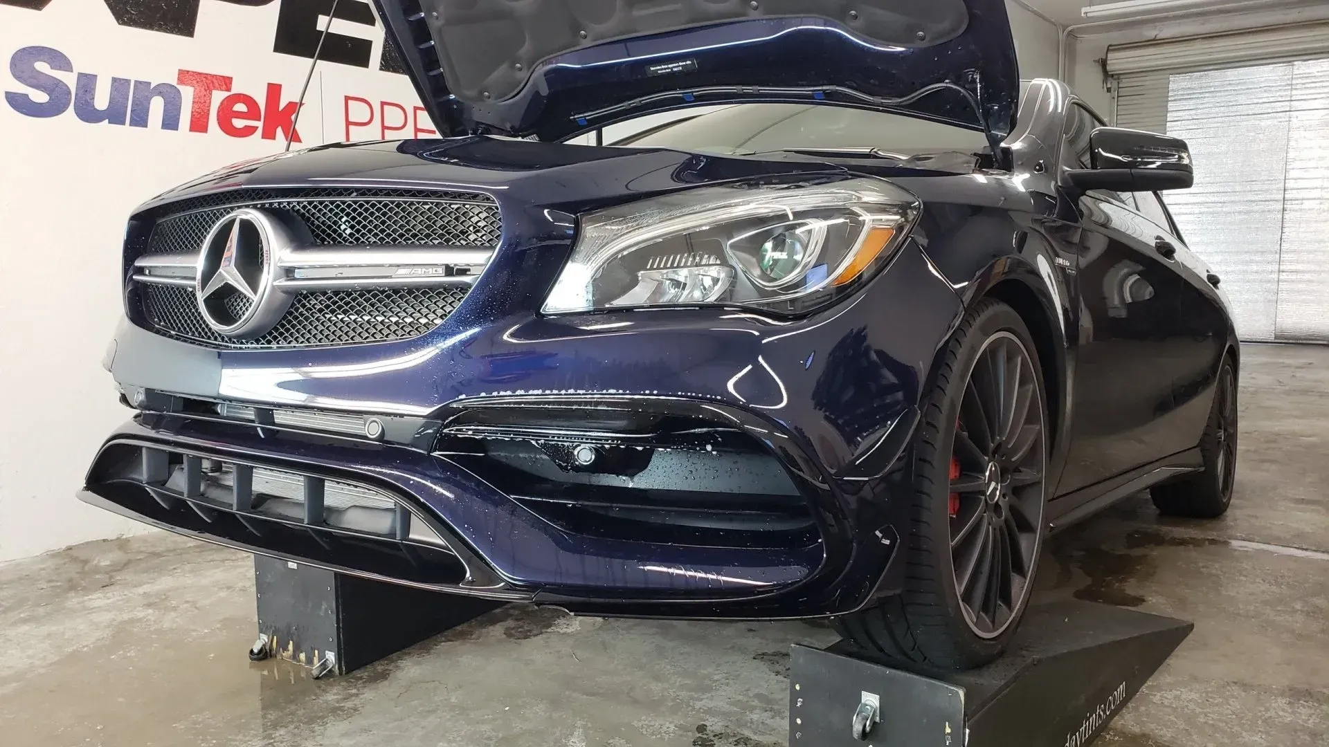 A blue mercedes benz with the hood up is sitting on a ramp.