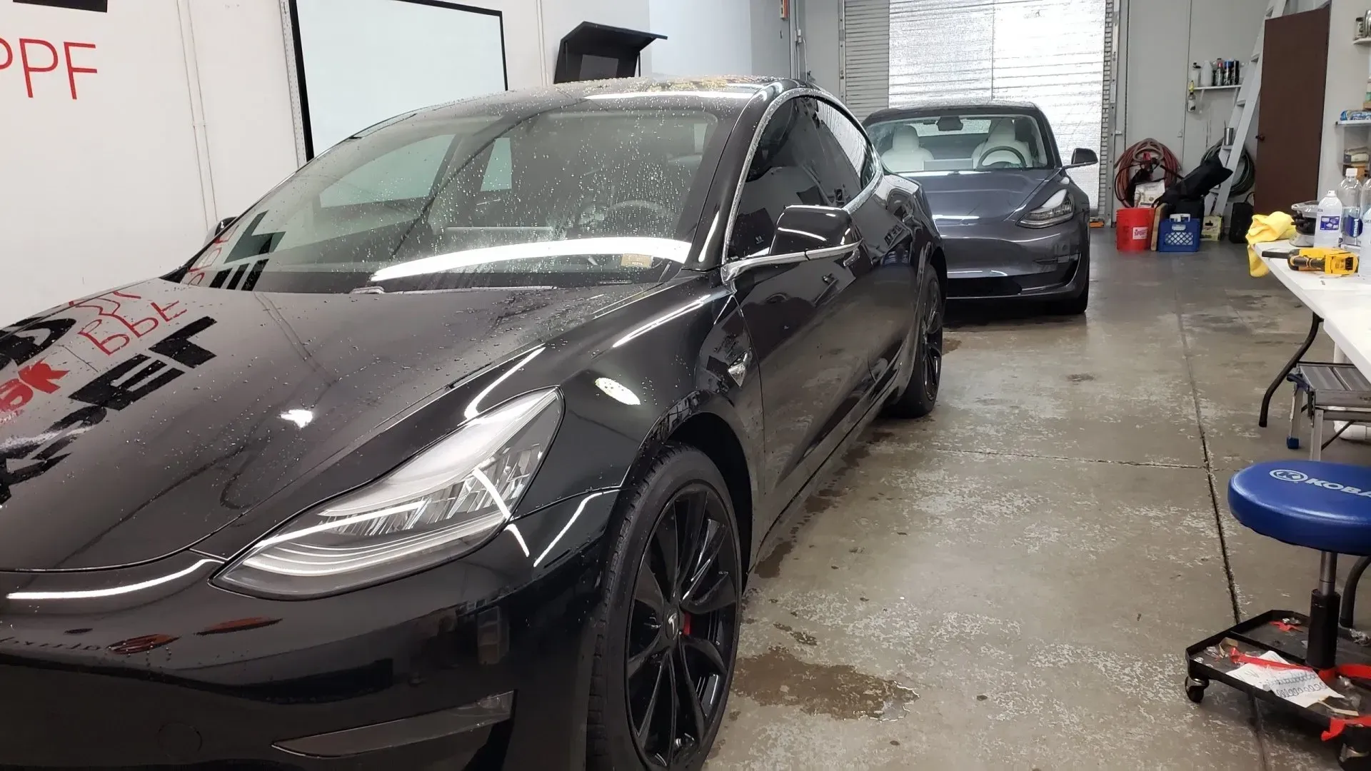 Two tesla model 3 cars are parked in a garage.