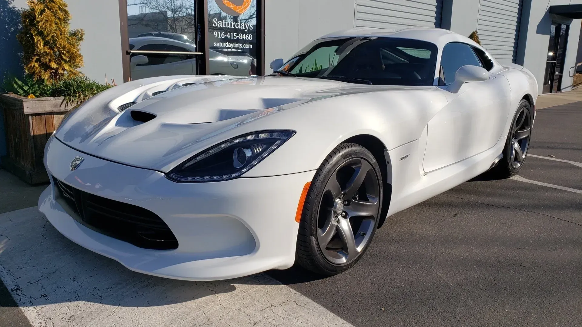 A white dodge viper is parked in front of a building.