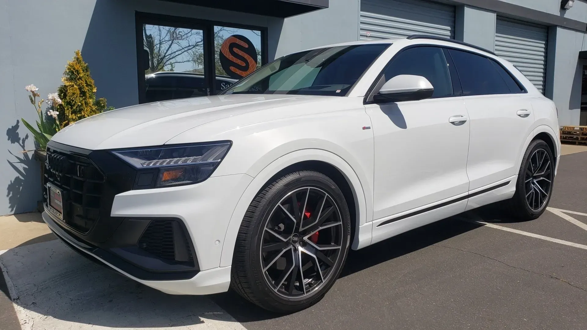 A white audi q8 is parked in a parking lot in front of a building.