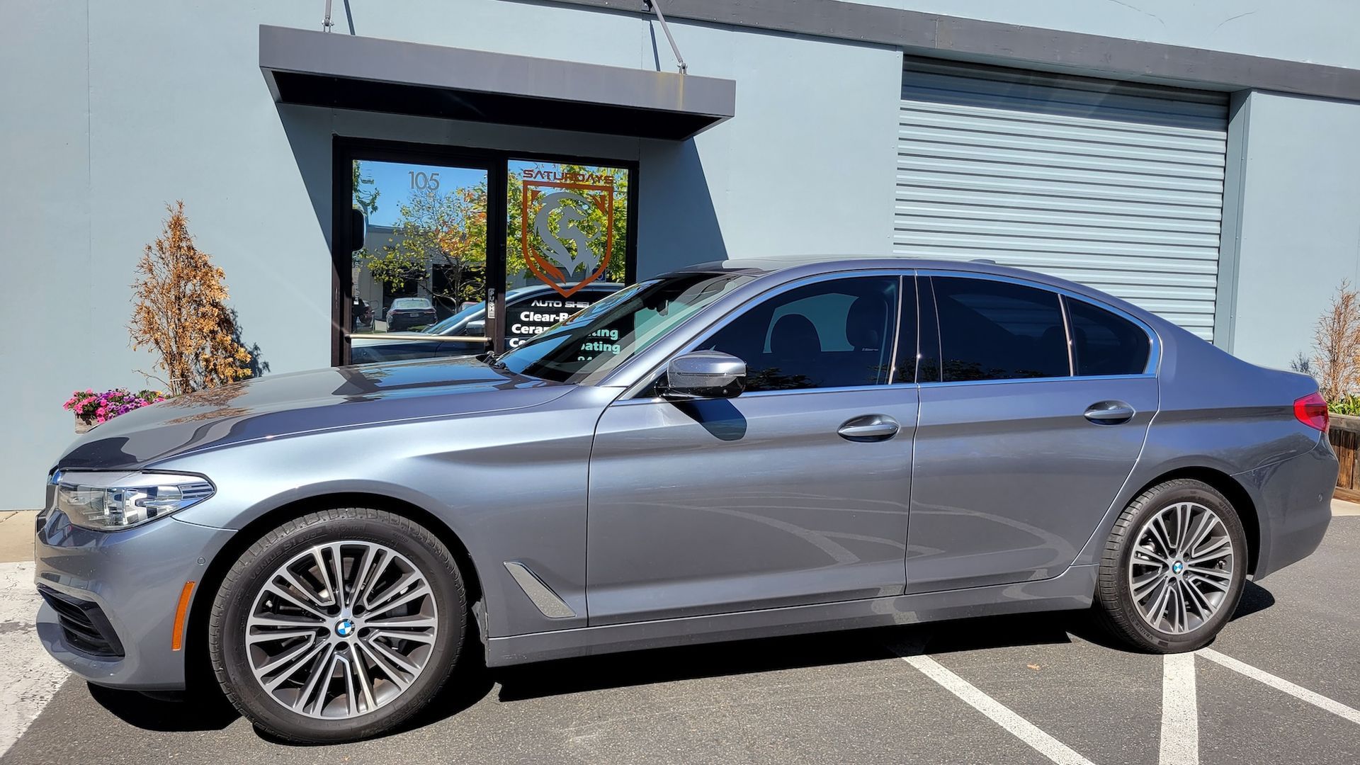 A gray bmw 5 series is parked in a parking lot in front of a building.