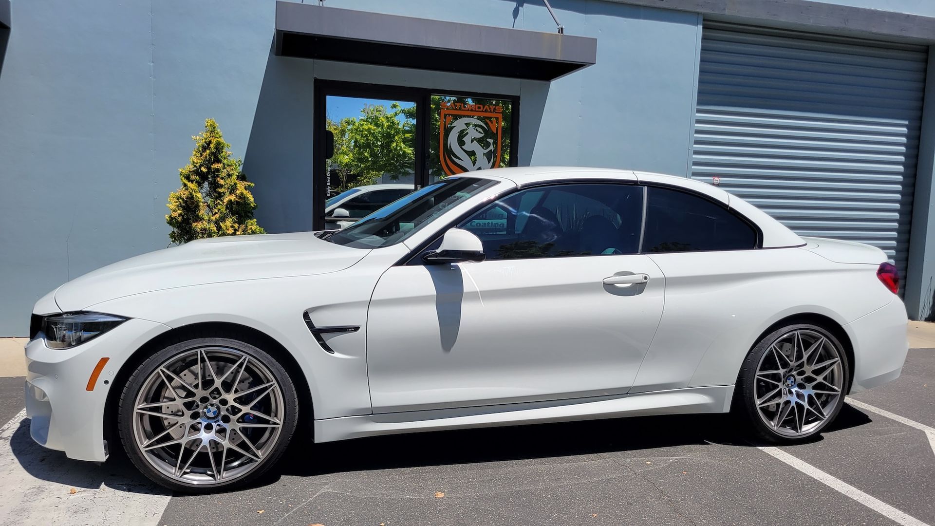 A white bmw m4 convertible is parked in front of a building.