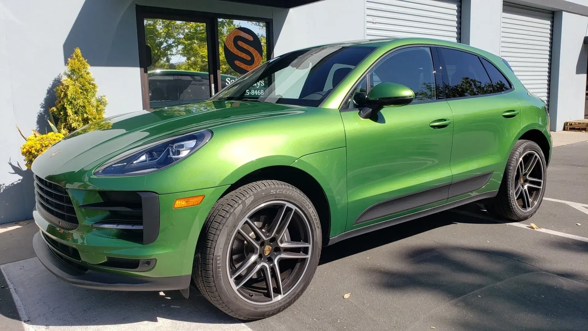 A green porsche macan is parked in a parking lot in front of a building.