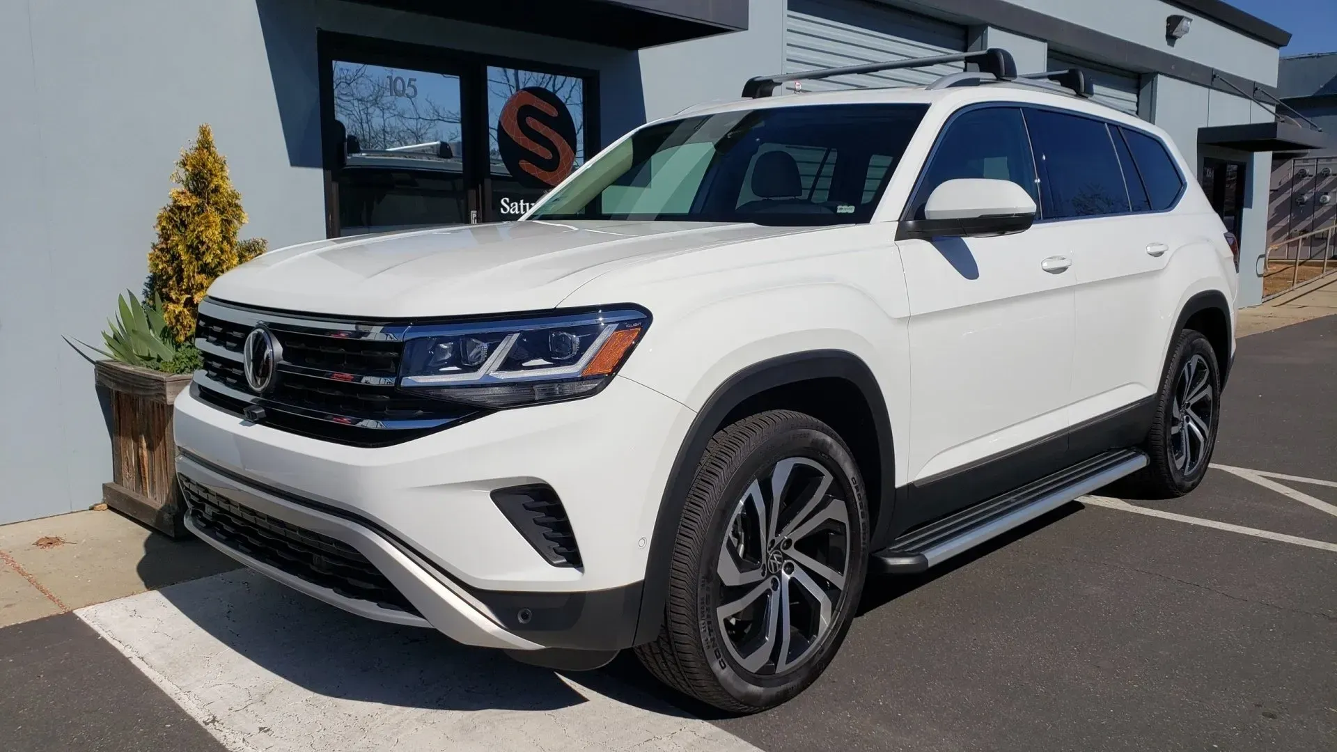 A white volkswagen atlas is parked in a parking lot in front of a building.