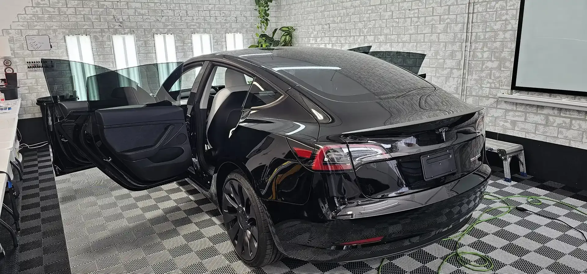A black tesla model 3 is parked in a garage with its doors open.