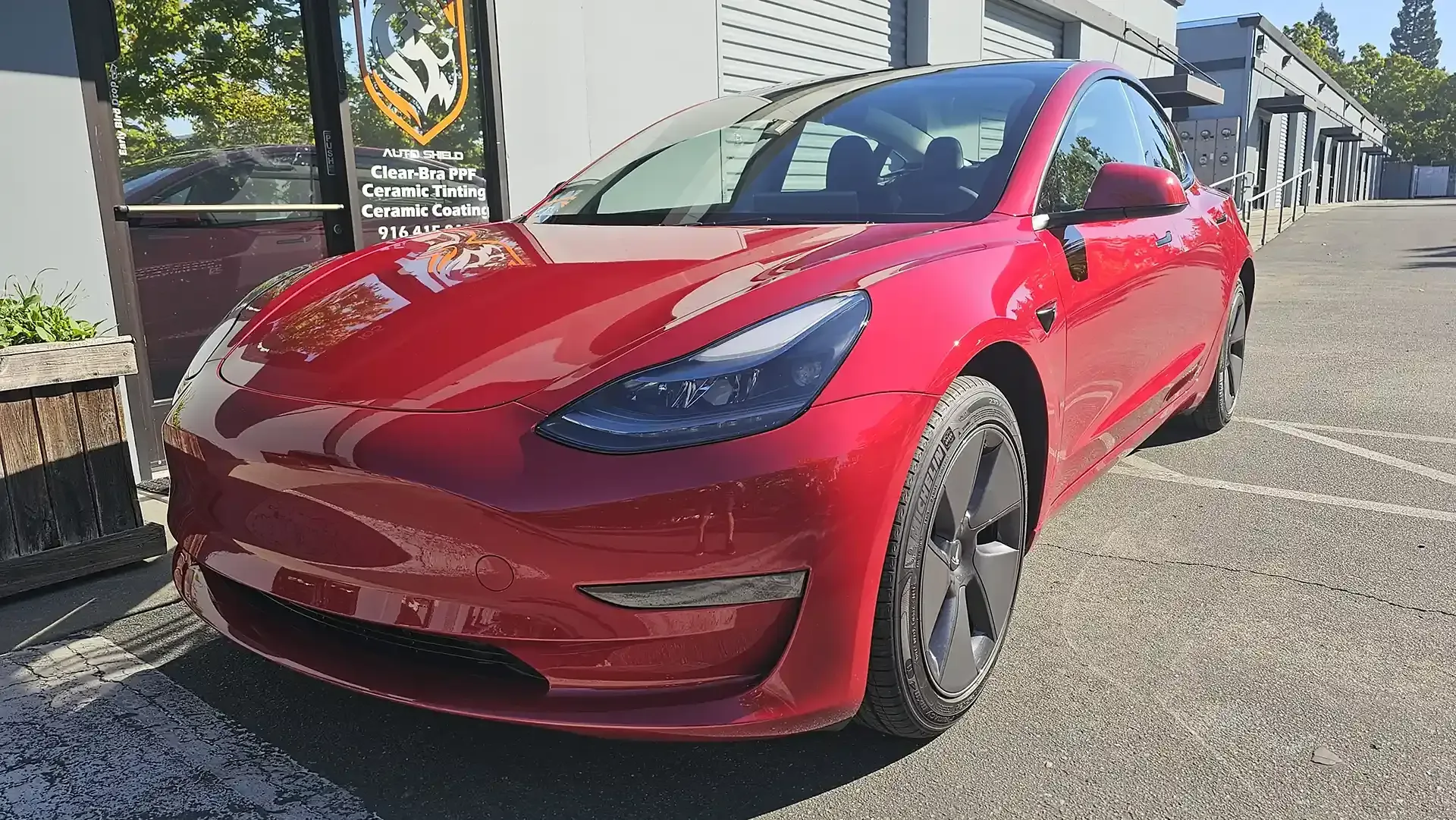 A red tesla model 3 is parked in a parking lot.