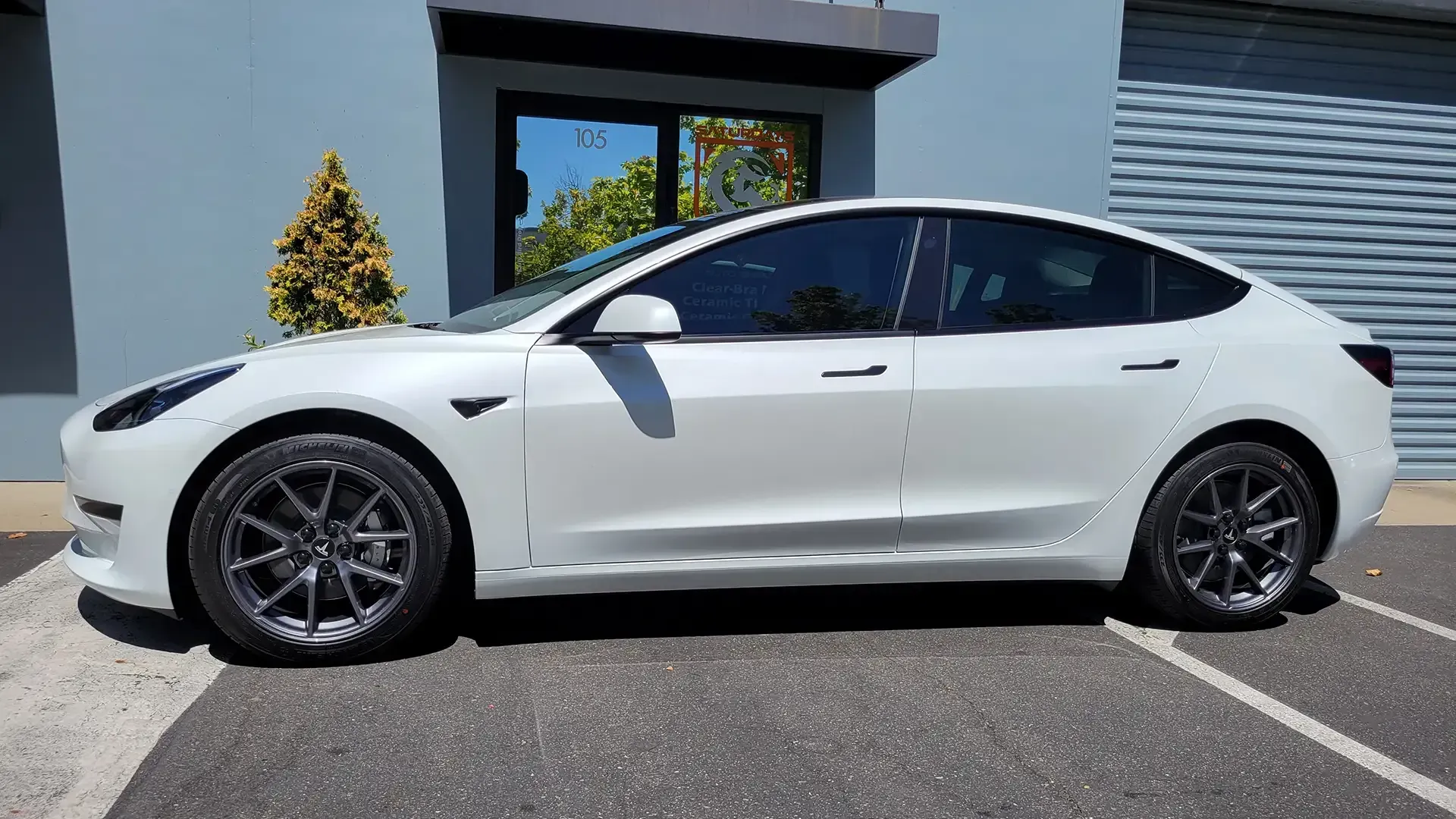 A white tesla model 3 is parked in a parking lot in front of a building.