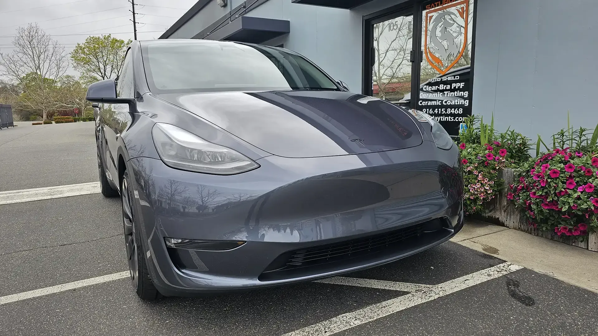 A tesla model y is parked in a parking lot in front of a building.