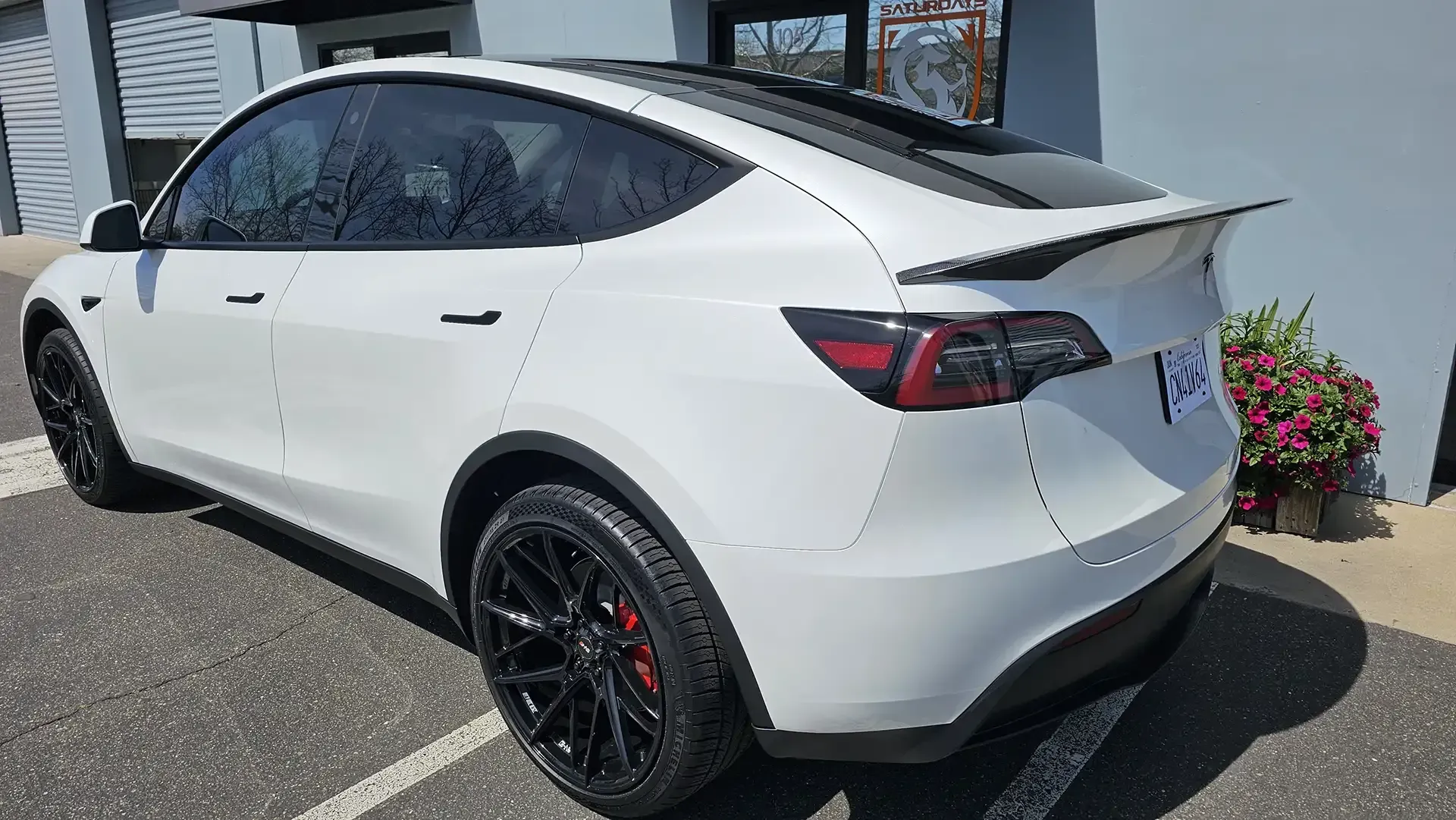 A white tesla model y is parked in a parking lot in front of a building.