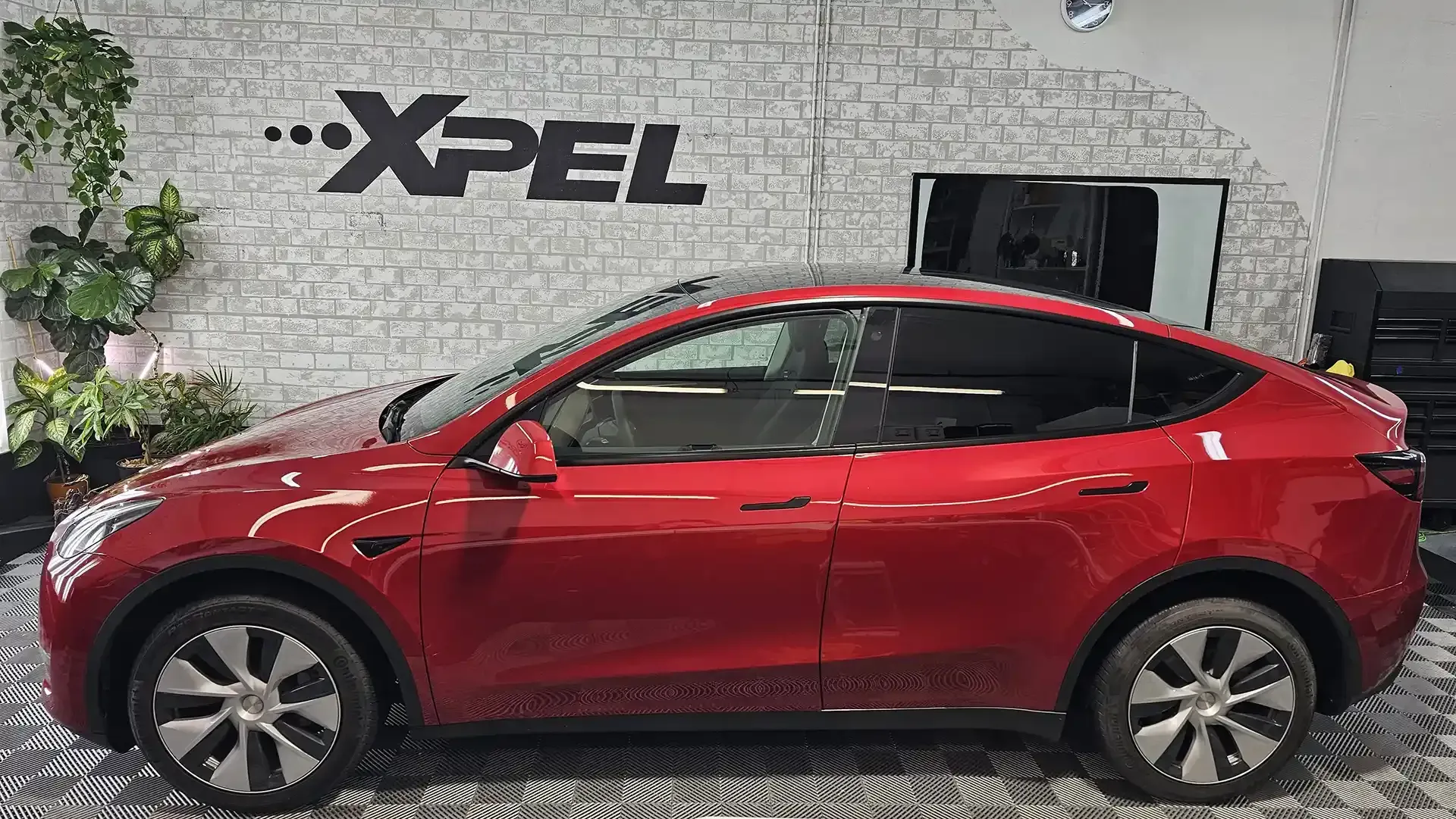 A red tesla model y is parked in front of a brick wall.