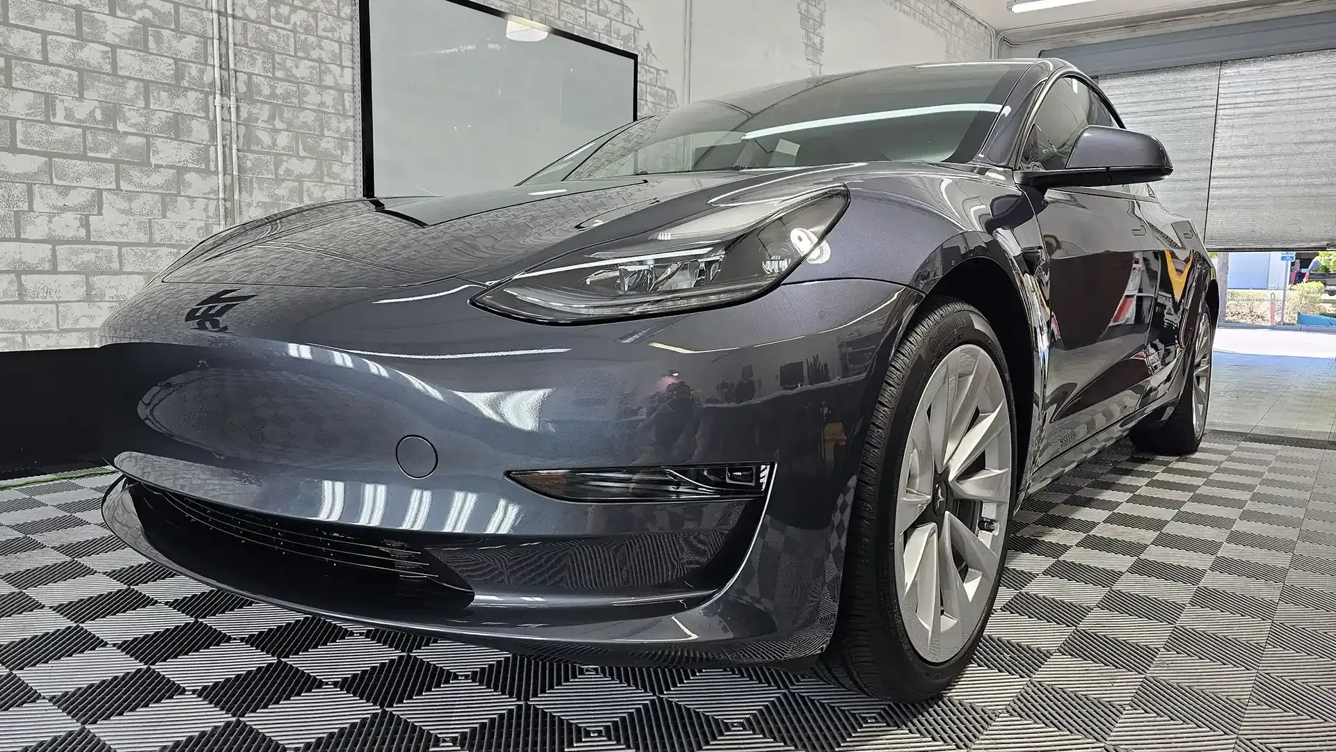A black tesla model 3 is parked in a garage.