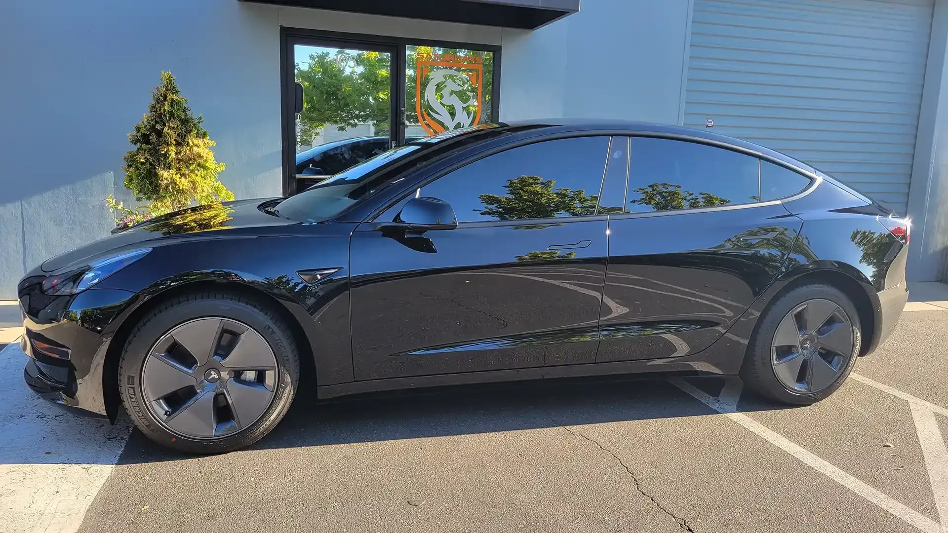 A black tesla model 3 is parked in a parking lot in front of a building.