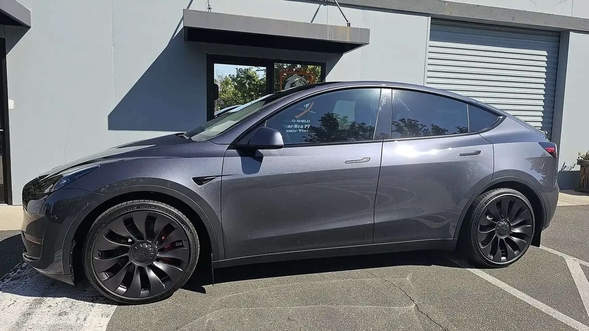 A tesla model y is parked in a parking lot in front of a building.