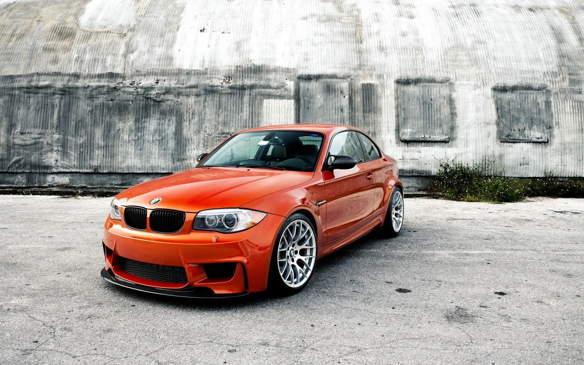 An orange bmw m1 is parked in front of a building.