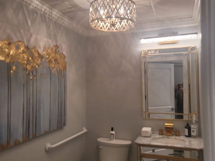 A bathroom with a toilet , sink , mirror and chandelier.