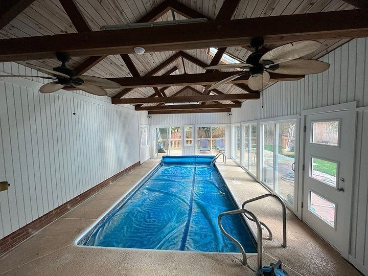 A large indoor swimming pool with a lot of windows and ceiling fans.