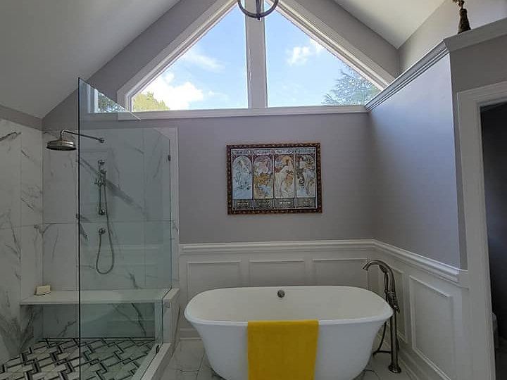 A bathroom with a bathtub , shower , and large window.