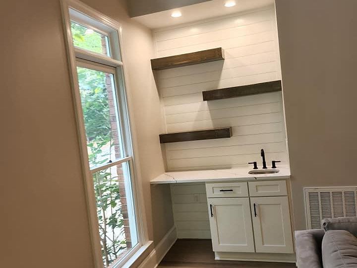 A living room with a sink , shelves and a window.