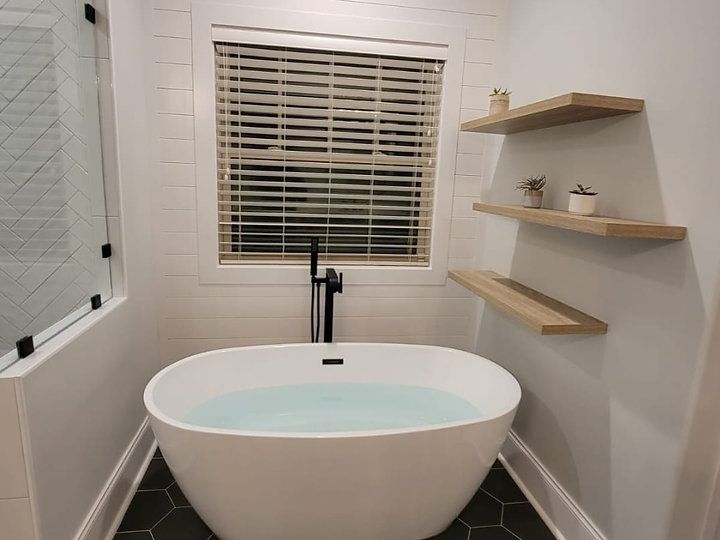 A bathroom with a bathtub , shelves and a window.