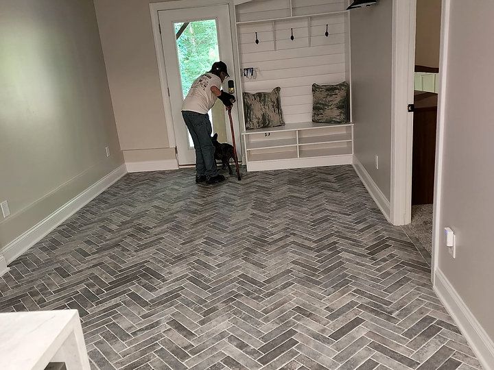 A woman is standing next to a dog in a room with a herringbone floor.