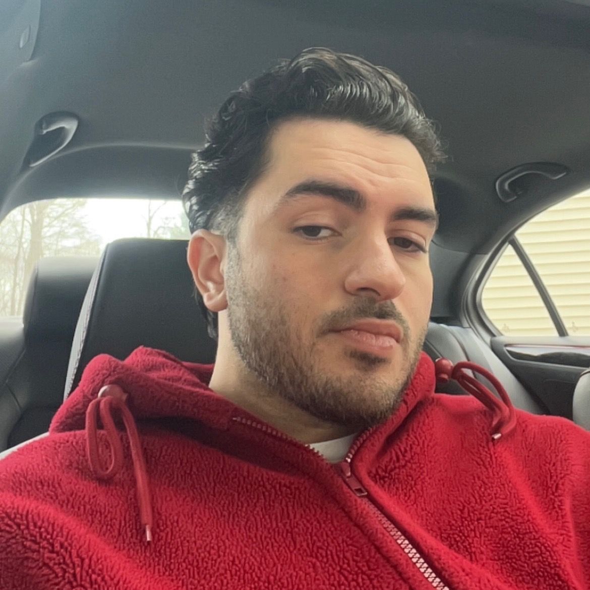 Man in red hoodie, looking slightly to the side, seated in a car.