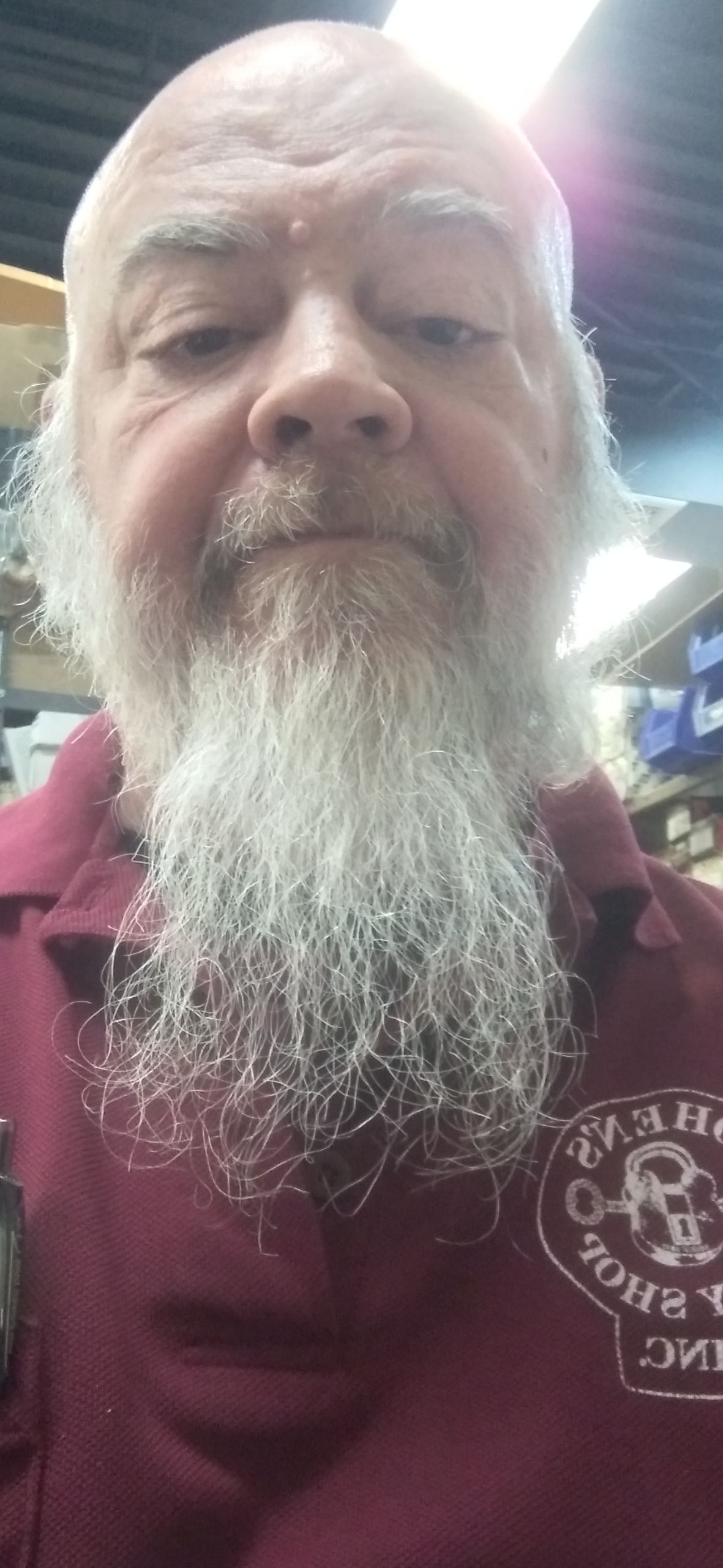 A man with a long white beard wearing a burgundy shirt with a logo.