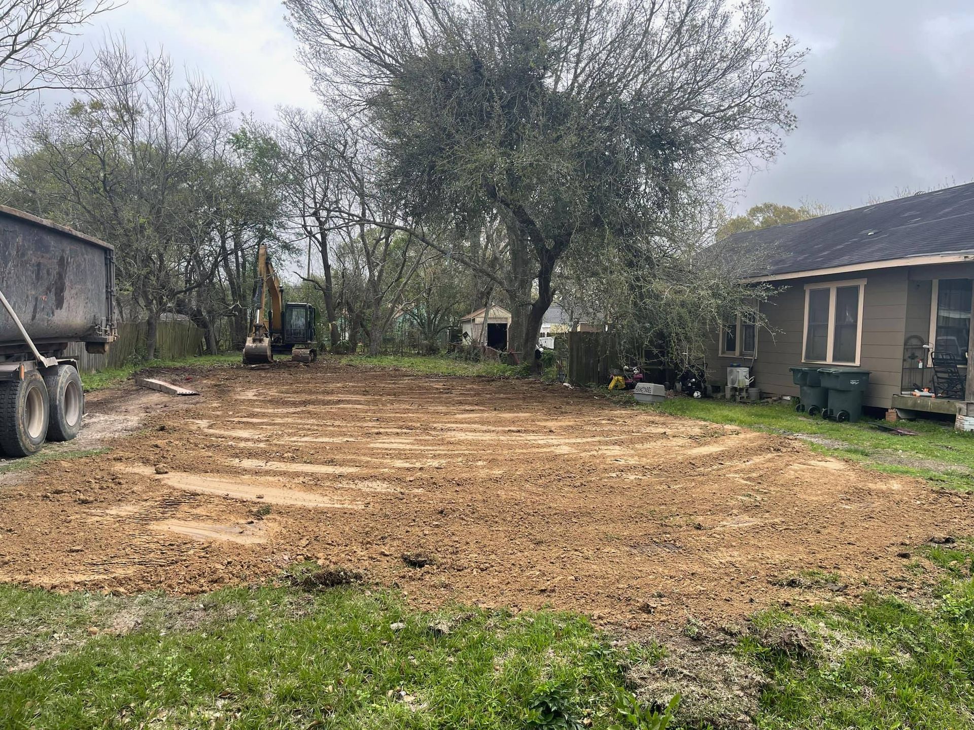 A dump truck is driving down a dirt road in front of a house.