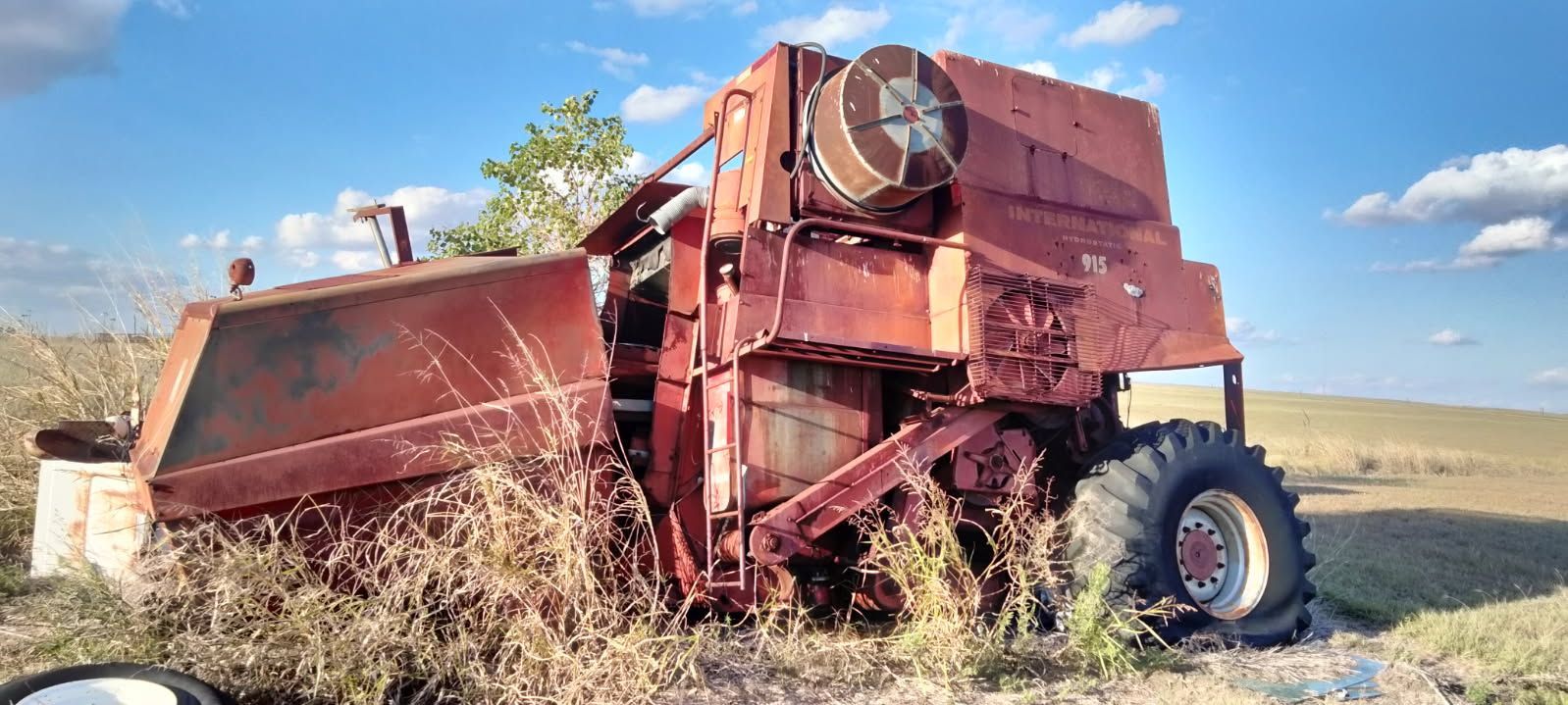 Rusty red combine harvester in a dry field under a blue sky, with a detached trailer beside it
