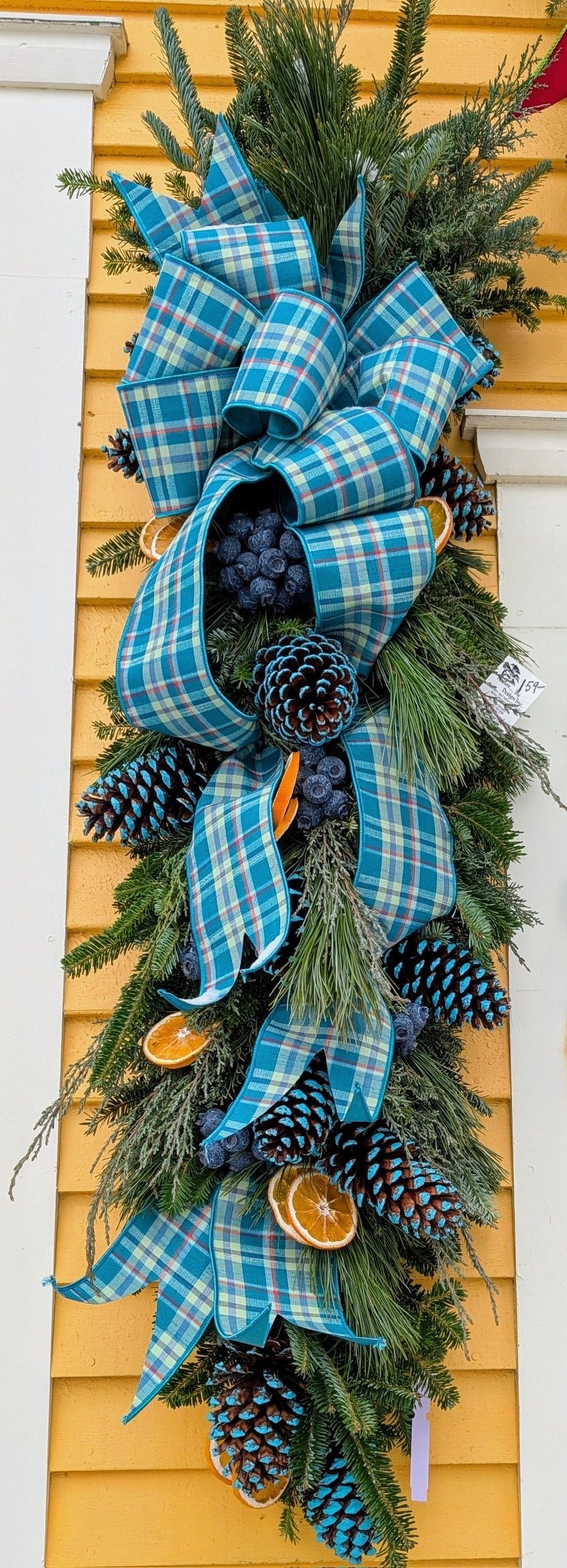 Blue plaid bow and greenery wreath with pinecones hanging on a wall