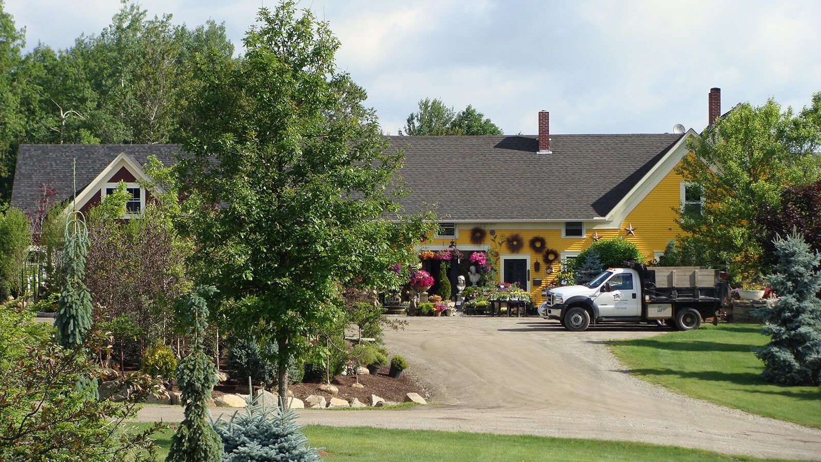 Suburban house with a yellow garage, trees, driveway, and a white pickup truck in front