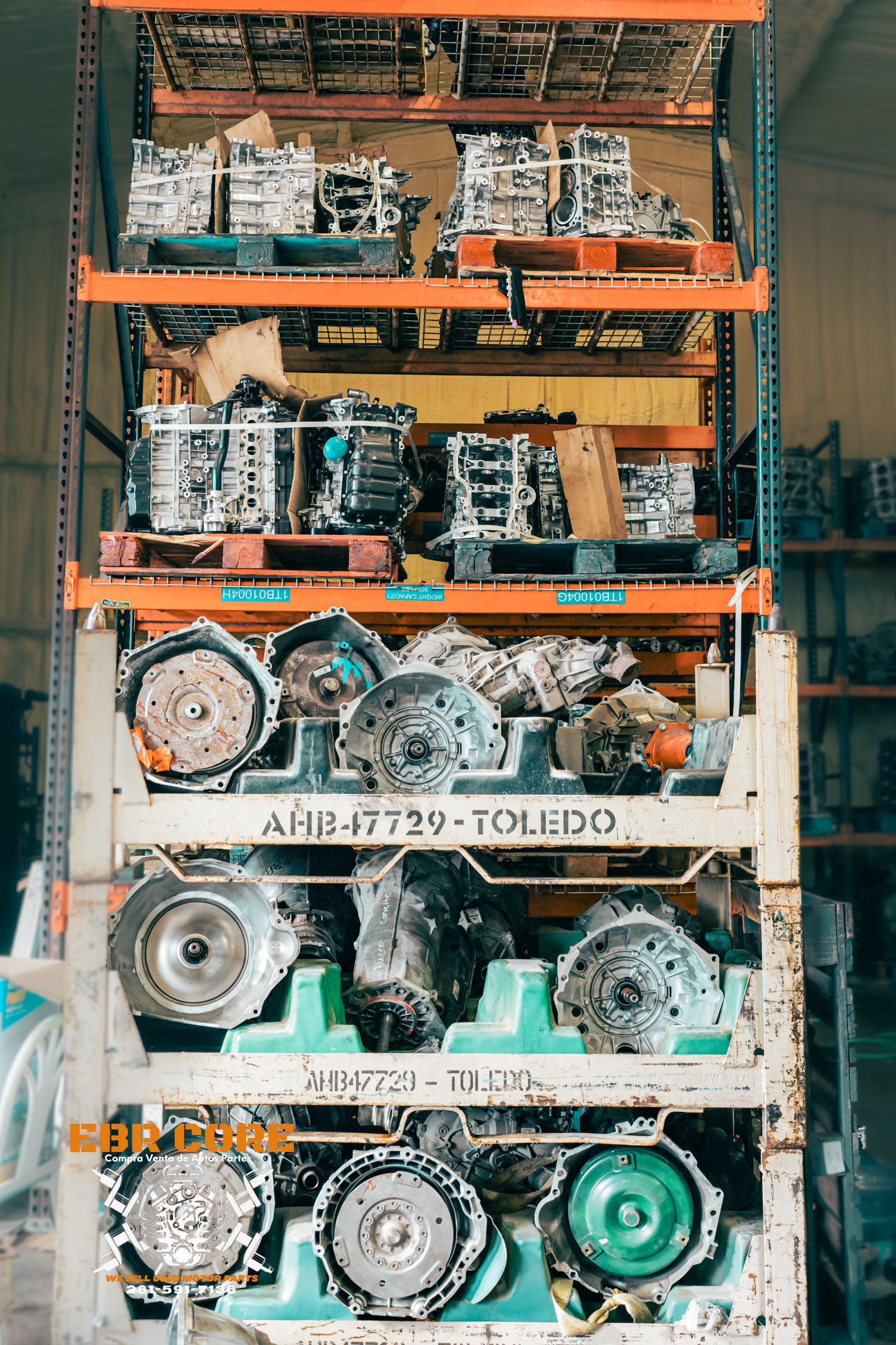 Automotive parts stacked on pallets inside a warehouse; various metal gears and engines displayed.
