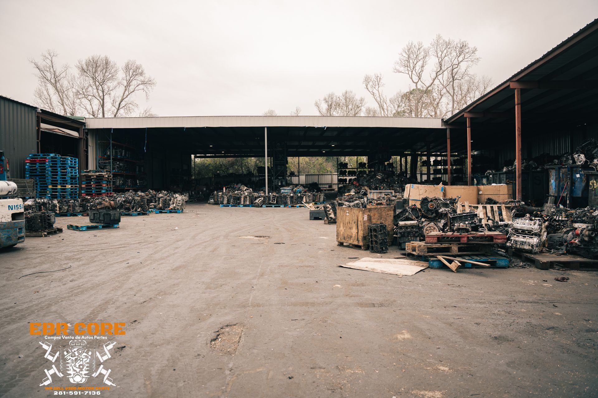 A large, cluttered auto parts yard with piles of engines, metal, and machinery under a covered structure.