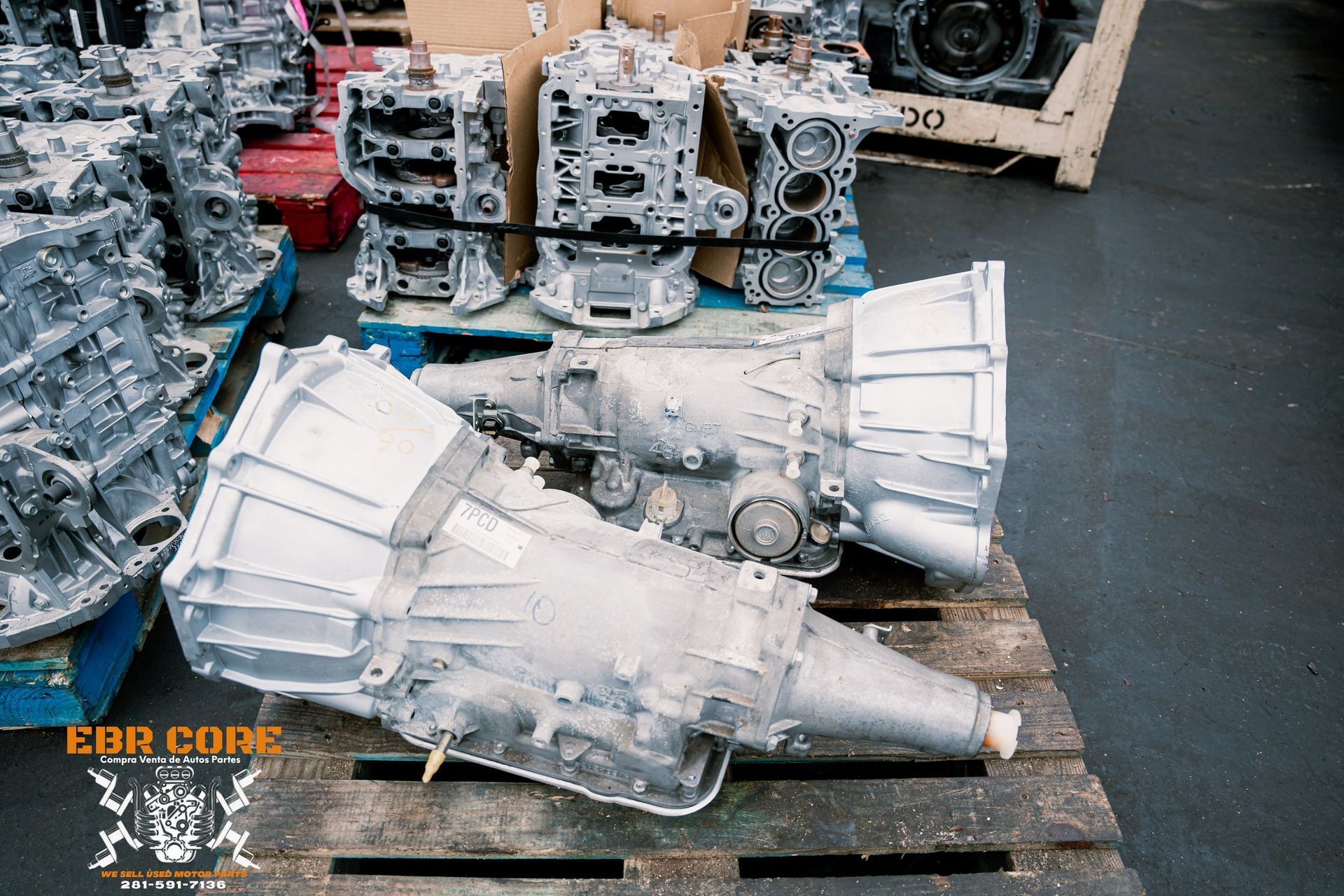 Two silver car transmissions and engine blocks on a wooden pallet, possibly for salvage or repair.