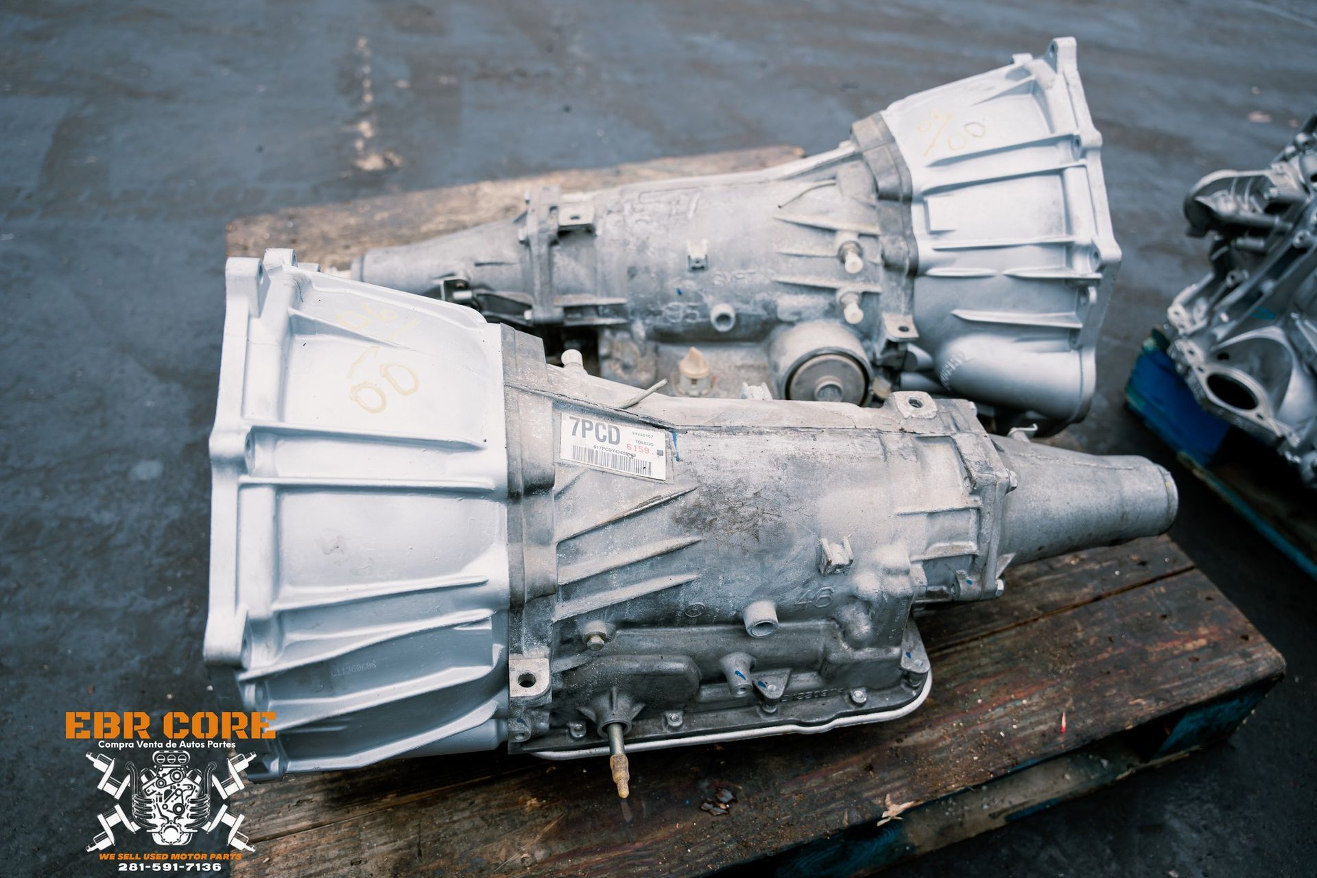 Two used automatic transmissions on a wooden pallet, outdoors. They have metal casings.