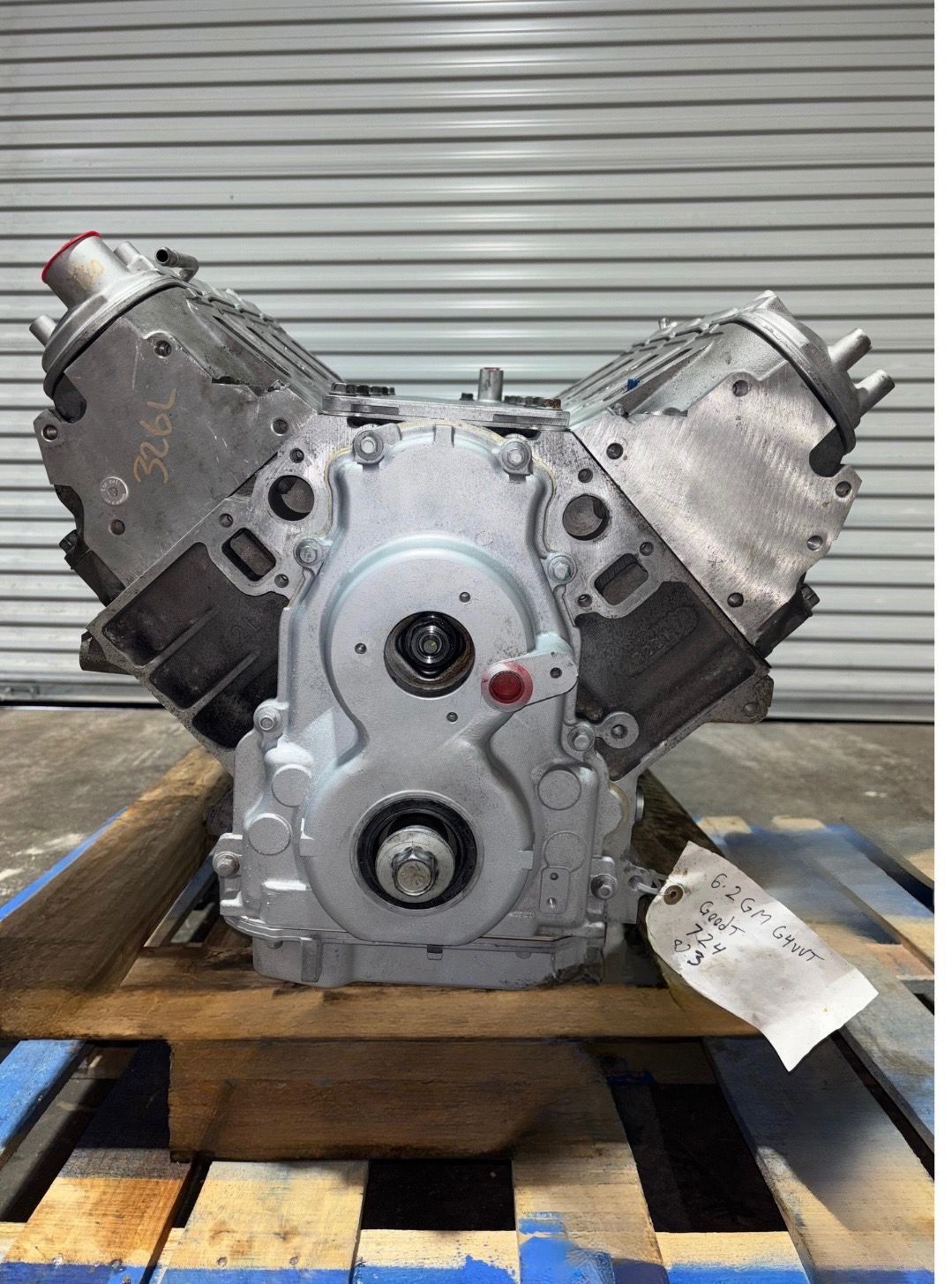 Silver V8 engine on wooden pallet, against a corrugated metal background.
