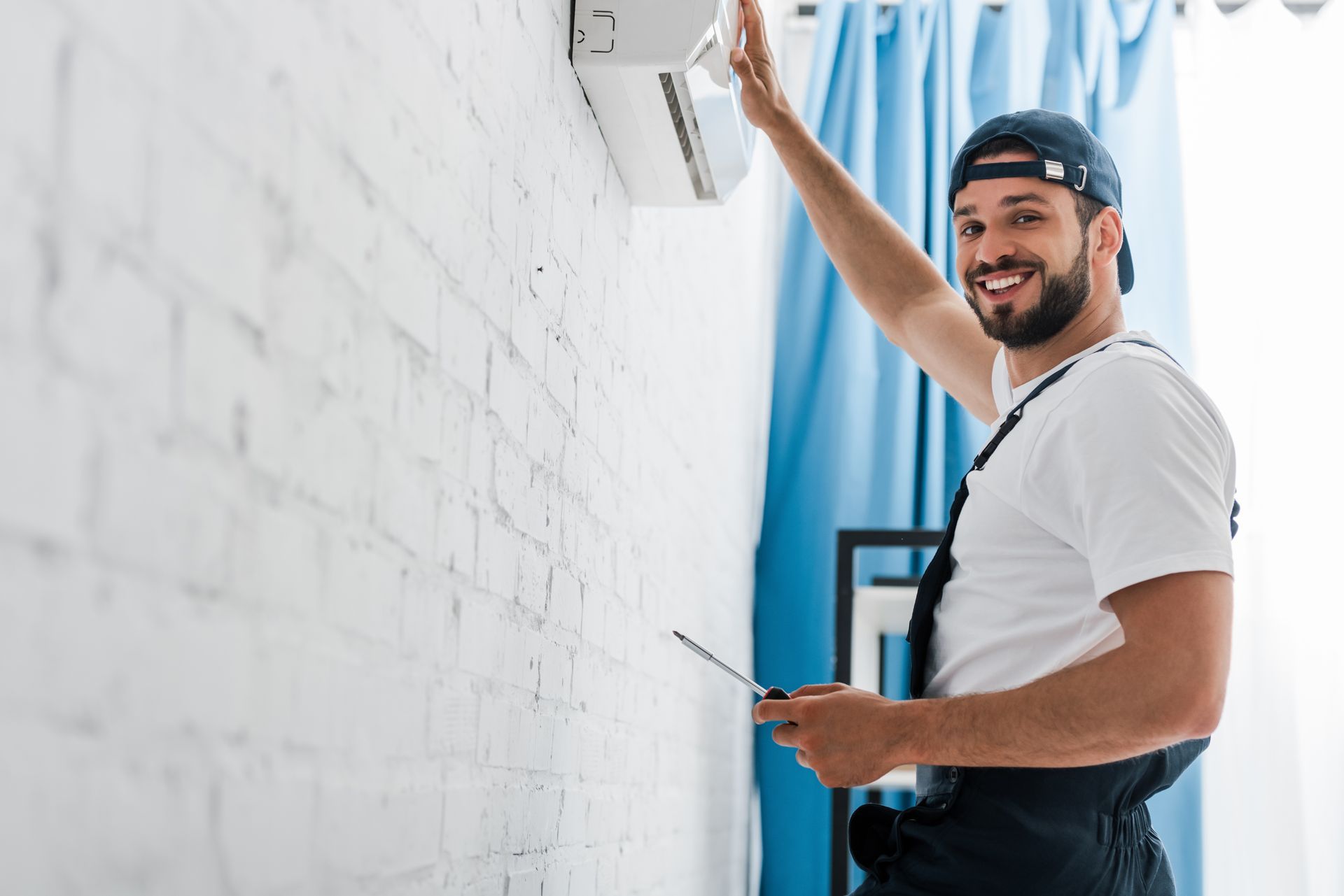 Smiling workman looking at camera while repairing air conditioner. Smiling workman looking at camera while repairing air conditioner.