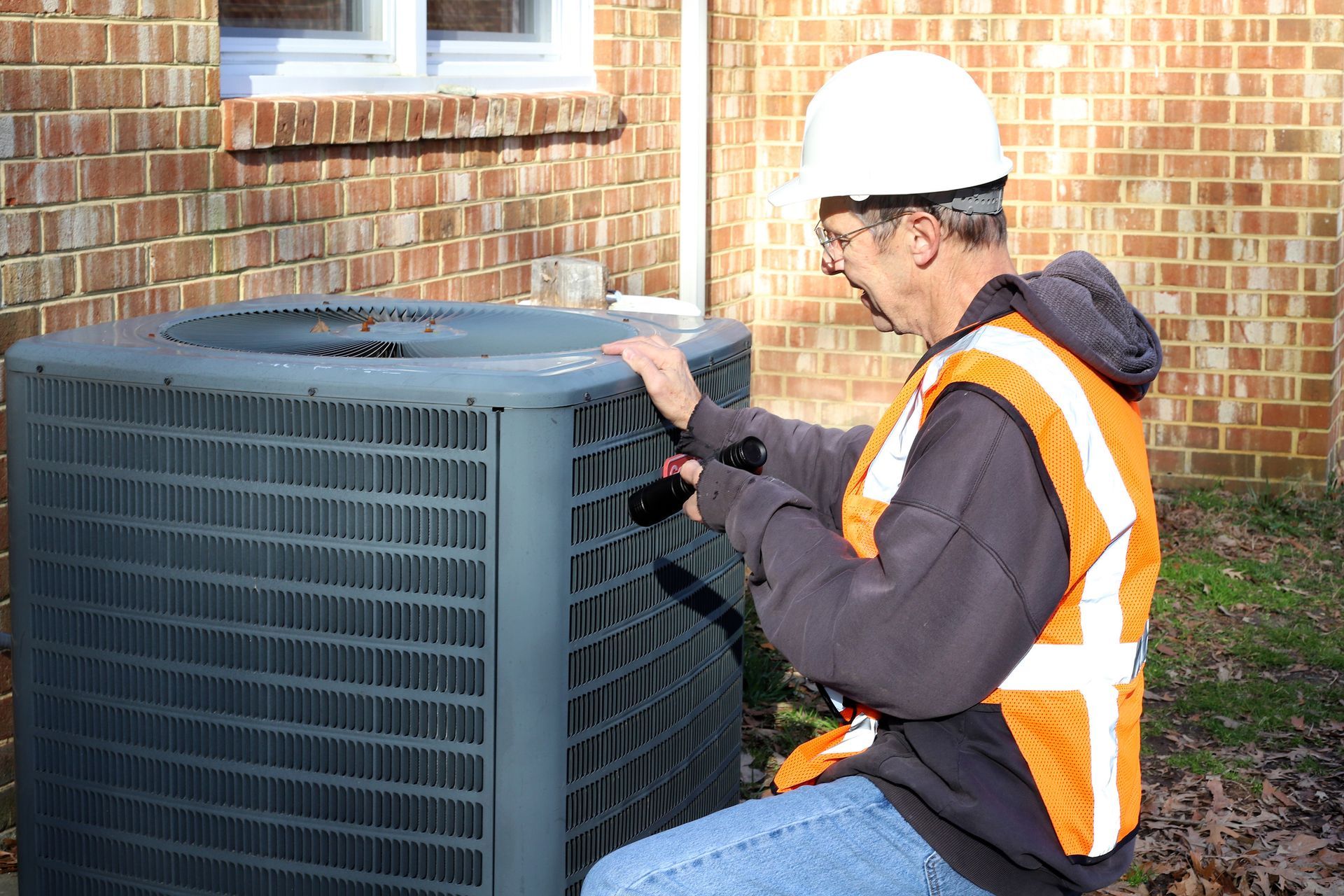 A Worker is inspecting an outdoor AC unit near a brick wall.]