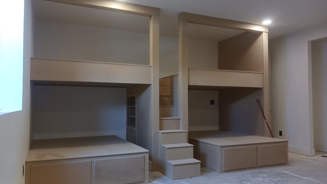 Built-in bunk beds with storage and stairs, unfinished wood in a room.