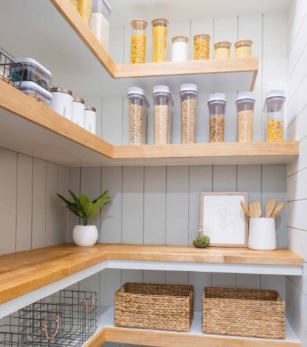 Well-organized pantry with wooden shelves, canisters, and baskets. White and gray color scheme.