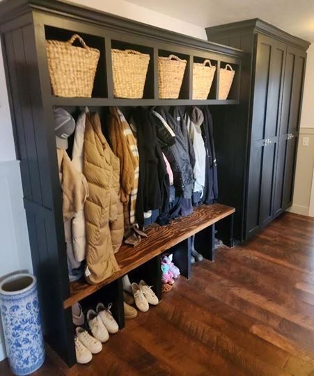 Black entryway cabinet with hanging coats, shoe storage, and wicker baskets; dark wood flooring.