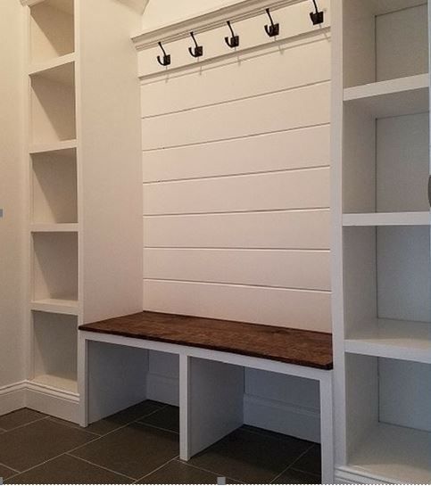 White built-in mudroom with shelves, bench, and hooks. Features white shiplap and a brown cushion.