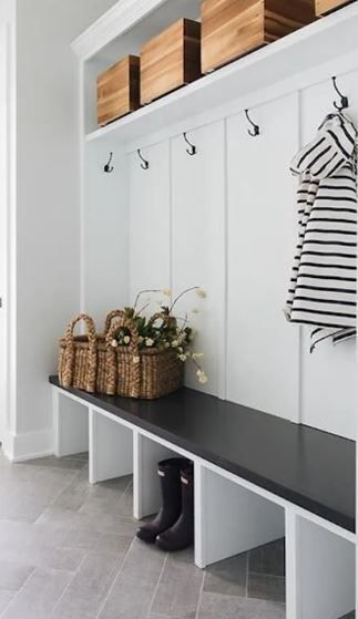 White entryway with built-in bench, hooks, storage, and wooden boxes. Black tabletop. Wicker baskets.