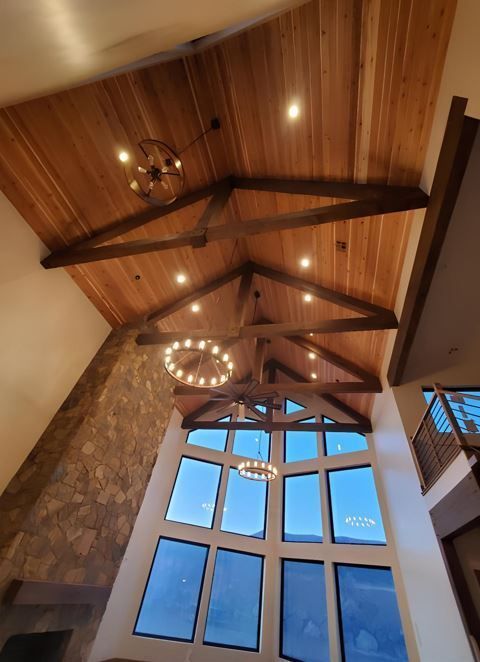 Wooden vaulted ceiling with star beams, chandeliers, and a large arched window in a stone-walled room