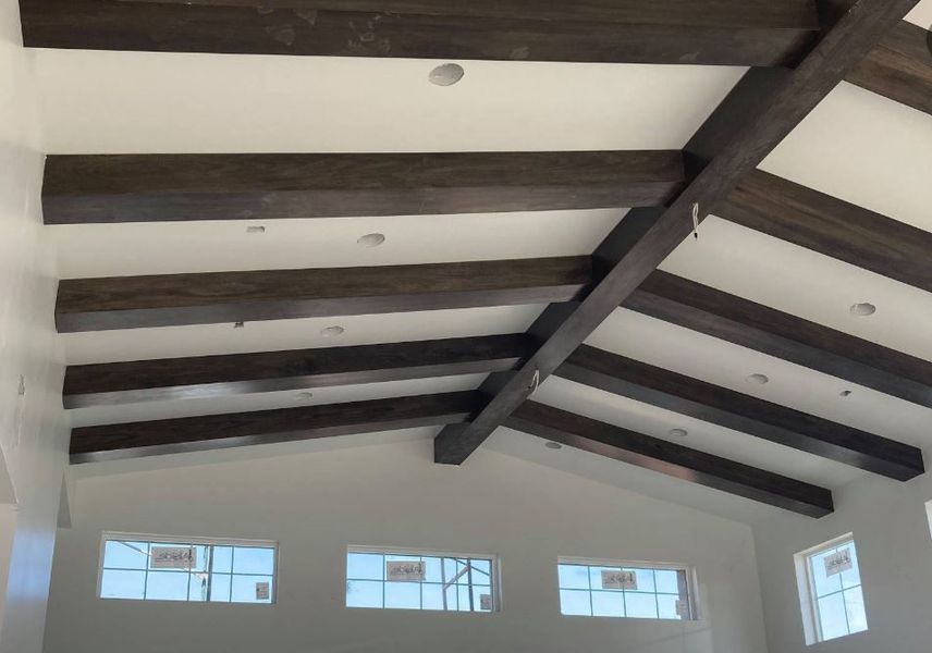 Angled white ceiling with dark wooden beams and recessed lights above windows.