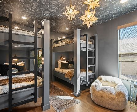 A modern bunk room with grey bunks, star lights, patterned ceiling, and a cozy bean bag chair.