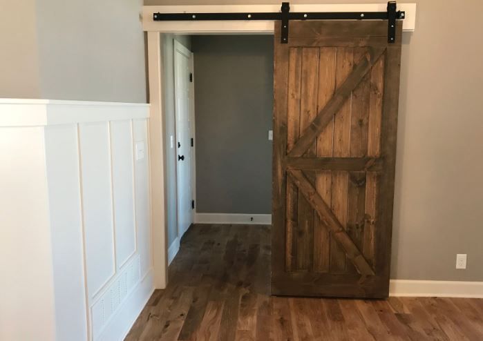 Barn door with rustic wood grain, open to a room with gray walls and wood flooring.