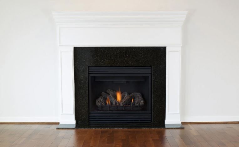 Fireplace with black interior and white mantel, set in a white wall above hardwood floor.