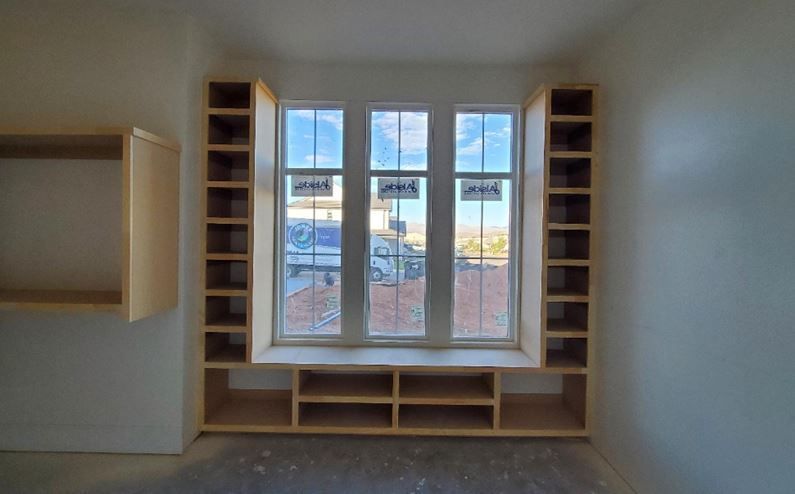 Window seat with built-in shelves on either side and below, in a room with white walls and an outdoor view.