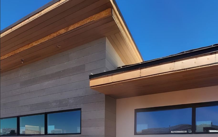 Modern building exterior with angled wood roof, stone siding, and dark-framed windows against a blue sky.